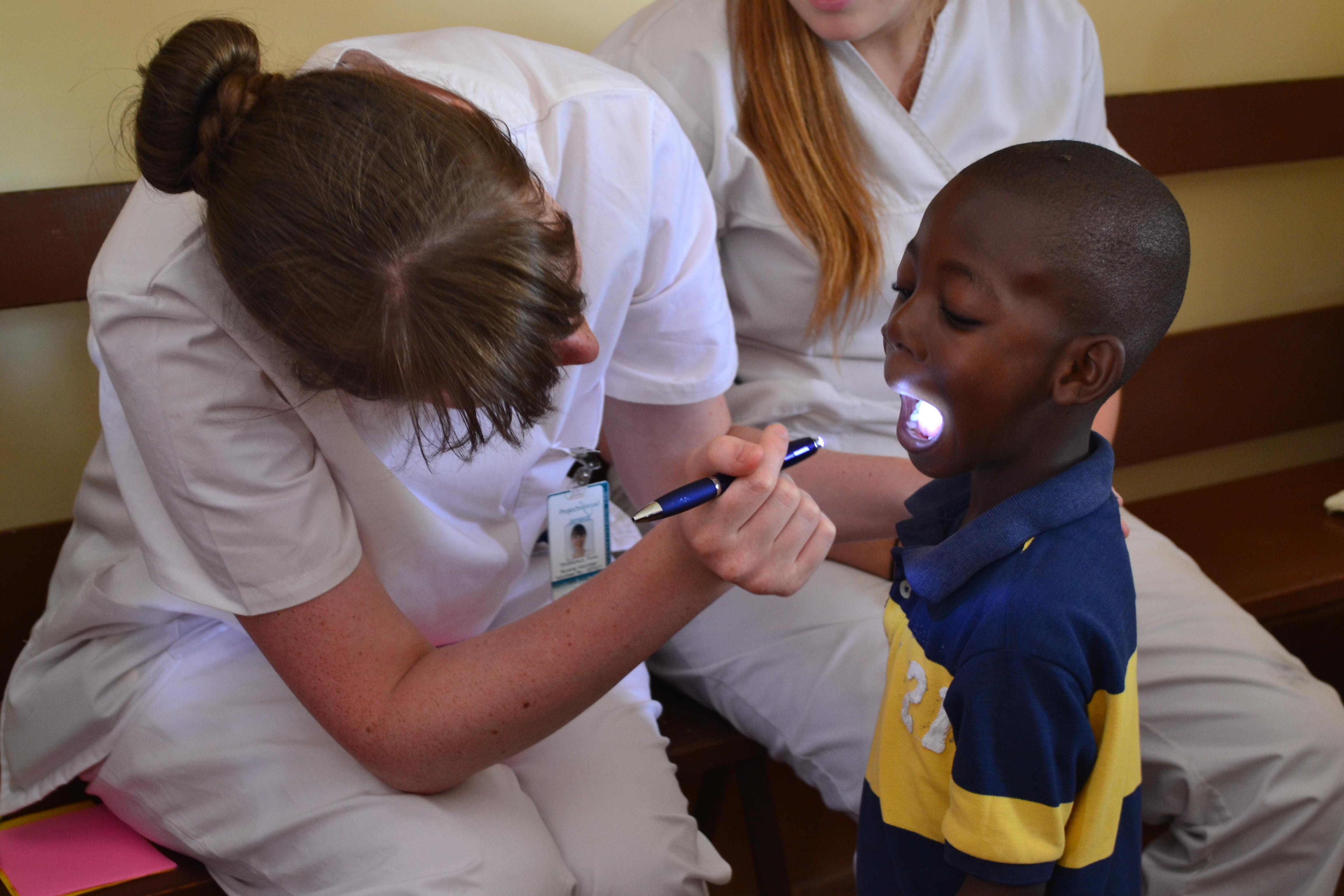 Female Medical volunteer examines a young childs mouth with a torch in a Heallthcare centre during an Outreach programme in Jamaica. Projects Abroad female Dentistry intern examines a childs mouth with a torch during an Outreach programme within a Dentistry placement in Jamaica.